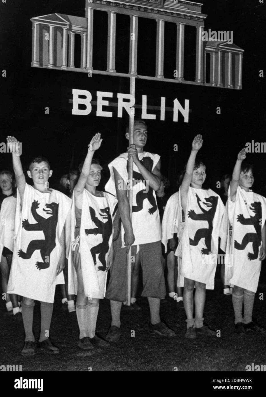 'During the movement game ''Deutscher Wille werde Licht!'' at the Festival of German Schools in the Grunewald Stadium, the herald group of the city of Berlin greets the crowd with the Nazi salute. The pupils wear the Berlin bear on their clothes and a sign with the Berlin landmark: The Brandenburg Gate.' Stock Photo