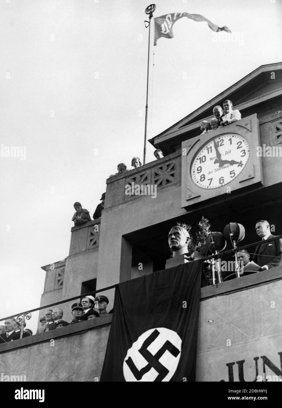 'At the ''Festival of the German School'' in Berlin's Grunewald Stadium, a bust of the absent Adolf Hitler is displayed in the VIP stand above a swastika flag. Over it is a clock, set according to the observatory's standard time. On a flagpole hangs a flag of the organizer ''Volksbund fuer das Deutschtum im Ausland'', VDA.' Stock Photo