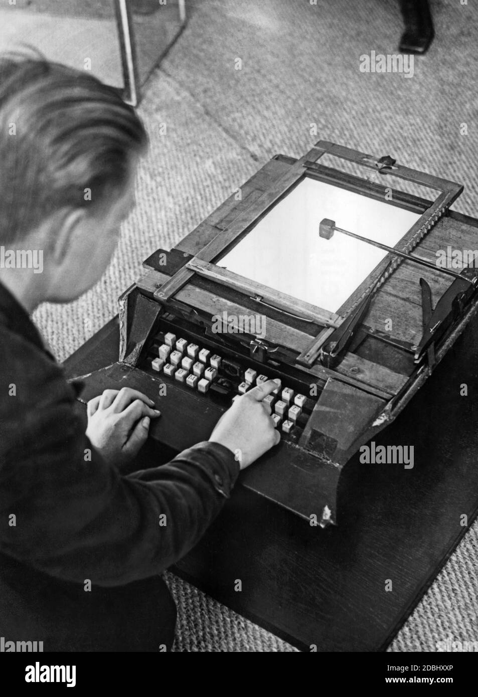 A boy writes on the first German typewriter. This was built in 1867 by the Tyrolean carpenter Mitterhofer and was improved continuously. The picture was taken at a trade fair or exhibition, probably in the 1930s. Stock Photo