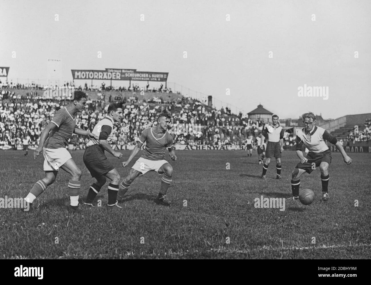 A soccer match between Bayern-Munich and Tennis-Borussia on the  Hertha-Platz am Gesundbrunnen in Berlin. The Bavarians win with 7 : 1. In  the background, the audience and big advertising banners for motorcycles