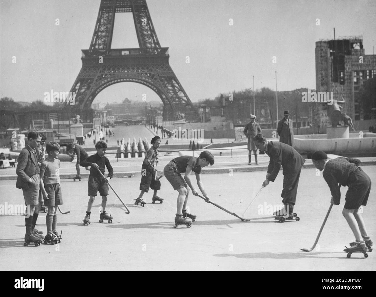 Some boys play field hockey on roller skates on the Place du Trocadero in front of the Eiffel Tower in Paris. On the right is the Trocadero Fountain, which has a statue of a bull in the middle. Stock Photo