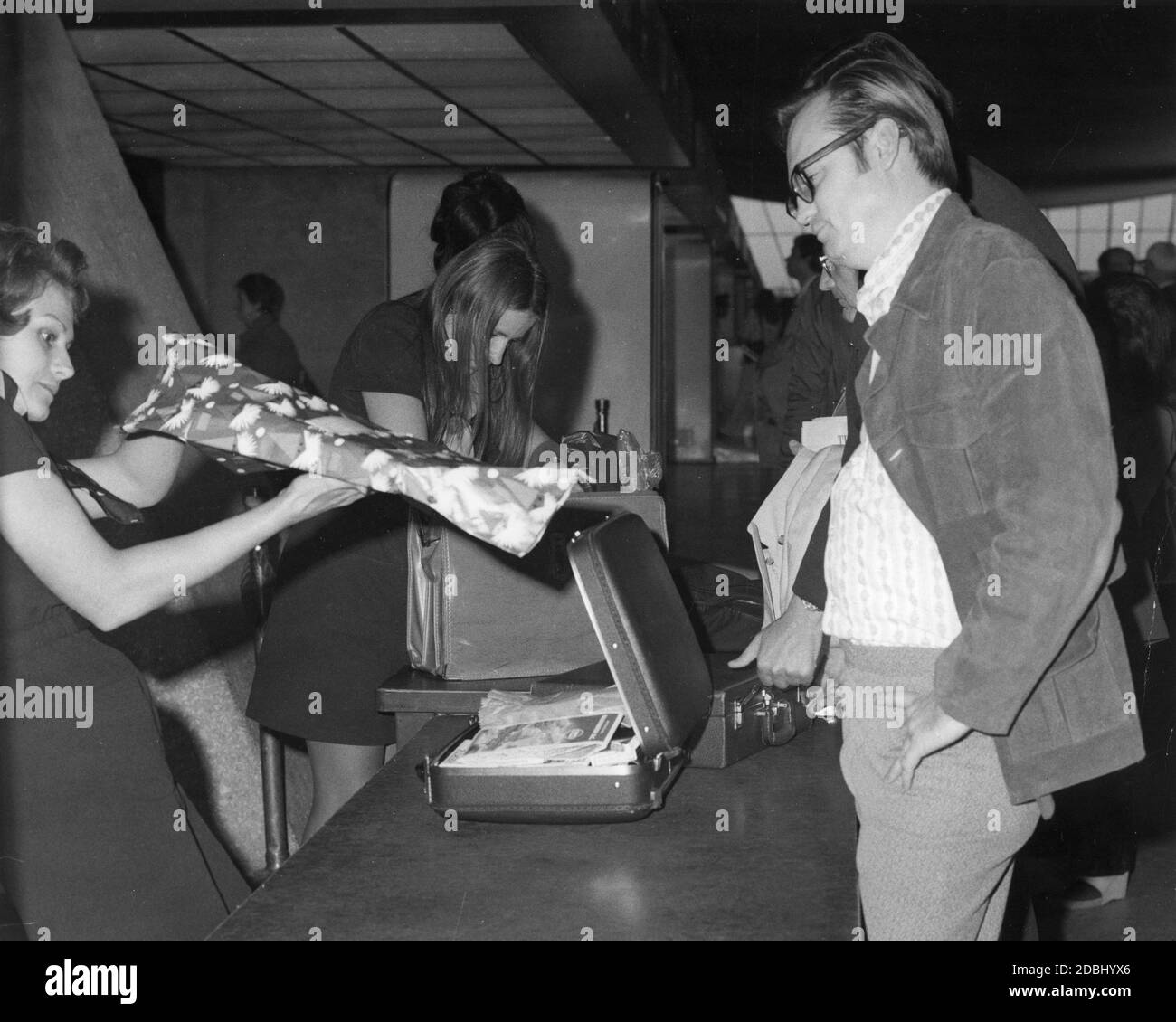 A traveler at Washington Dulles Airport looks on while airline personnel check his luggage and a Christmas gift for weapons and explosives, Chantilly, VA, circa 1975.  (Photo by Federal Aviation Administration/RBM Vintage Images) Stock Photo