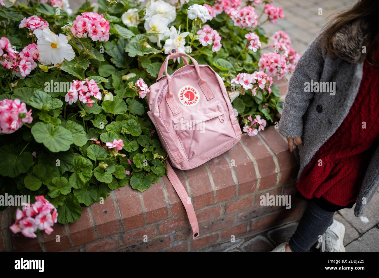 Pink backpack on top of flowers and plants next to a little girl Stock Photo