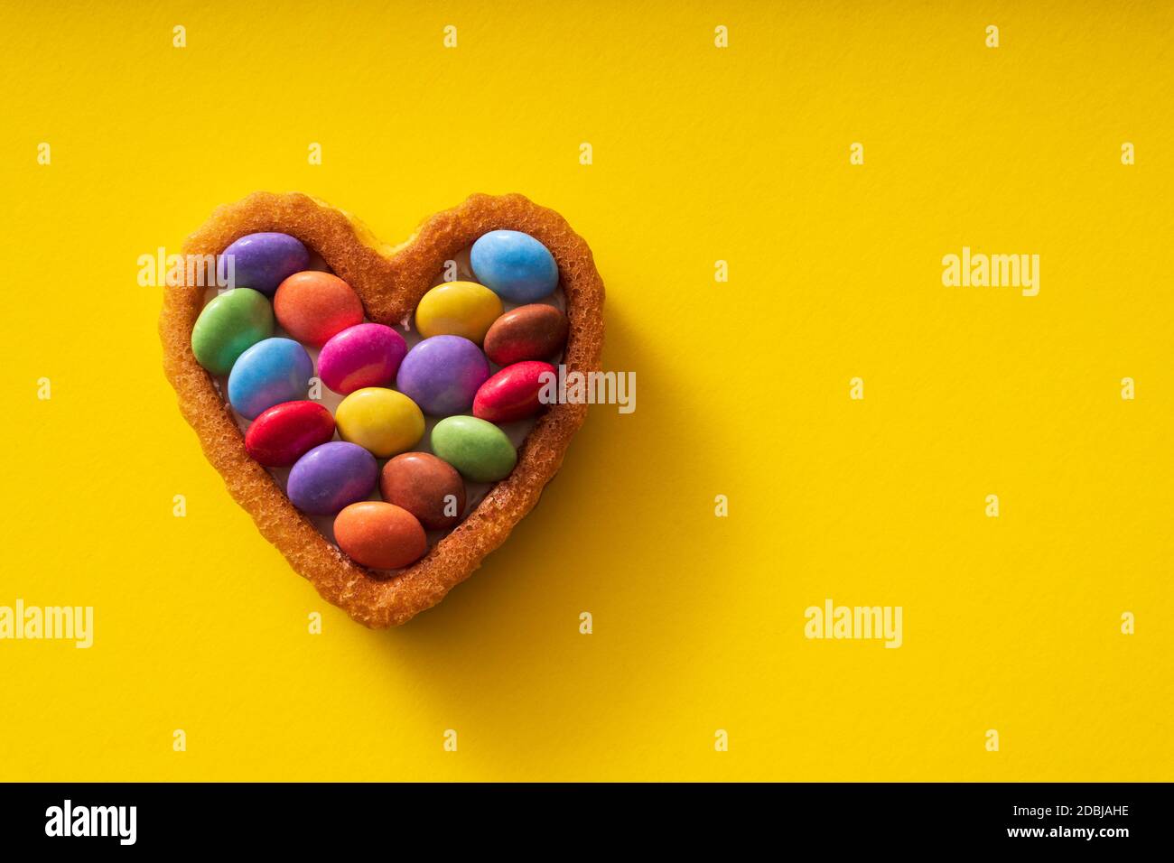 Colorful Candy Buttons on Heart shaped cake on yellow Background - Birthday concept Stock Photo