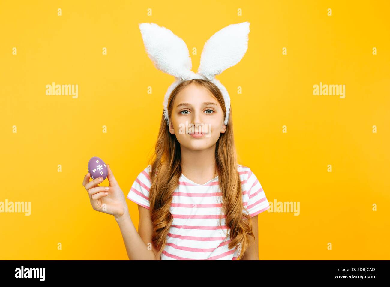 Beautiful happy girl on her head with rabbit ears and colorful Easter eggs in her hands, on a yellow background. Symbol of Easter and spring Stock Photo