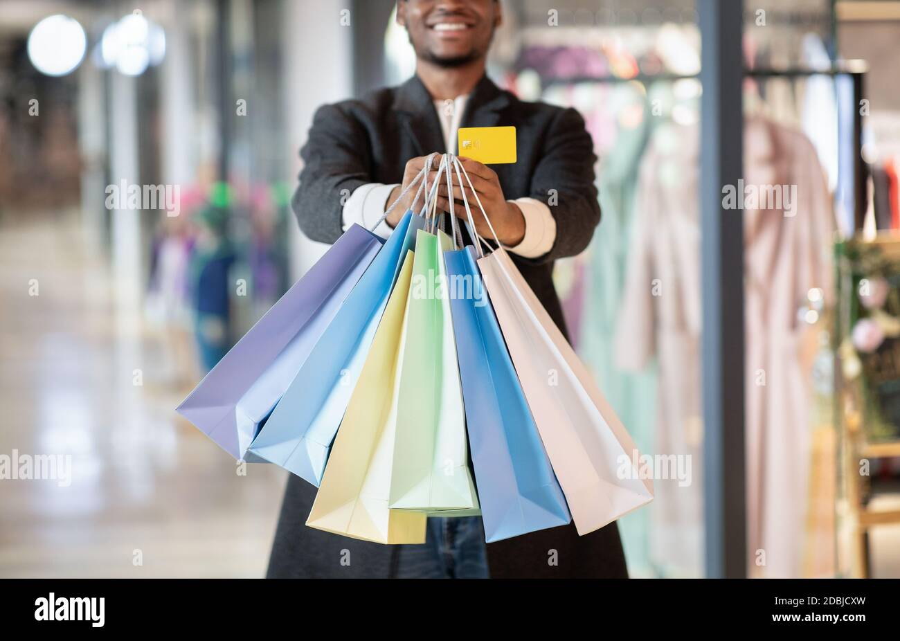 Young african american man expressing success, showing to camera of colored shopping bags and credit card Stock Photo