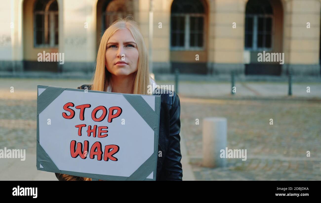 Young woman calling to stop the war by holding steamer. Protest walk in the city center. Stock Photo