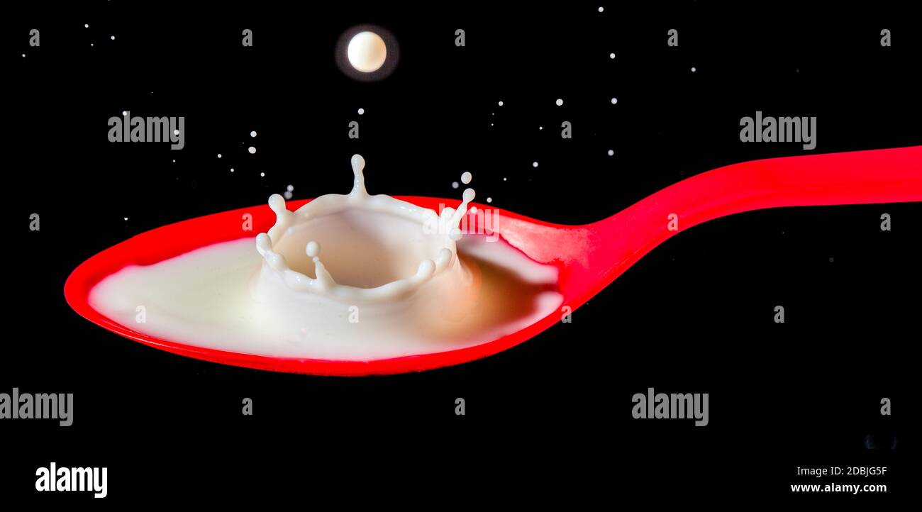 White milk splashing into red spoon Stock Photo