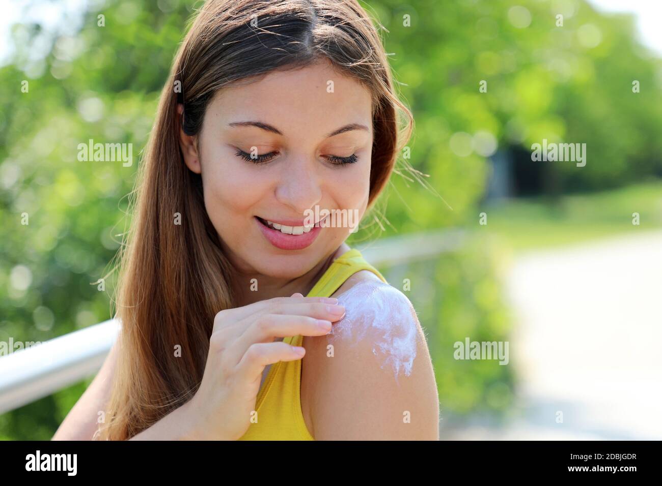 Happy young woman applying sunblock on shouder skin outdoor on a summer day Stock Photo