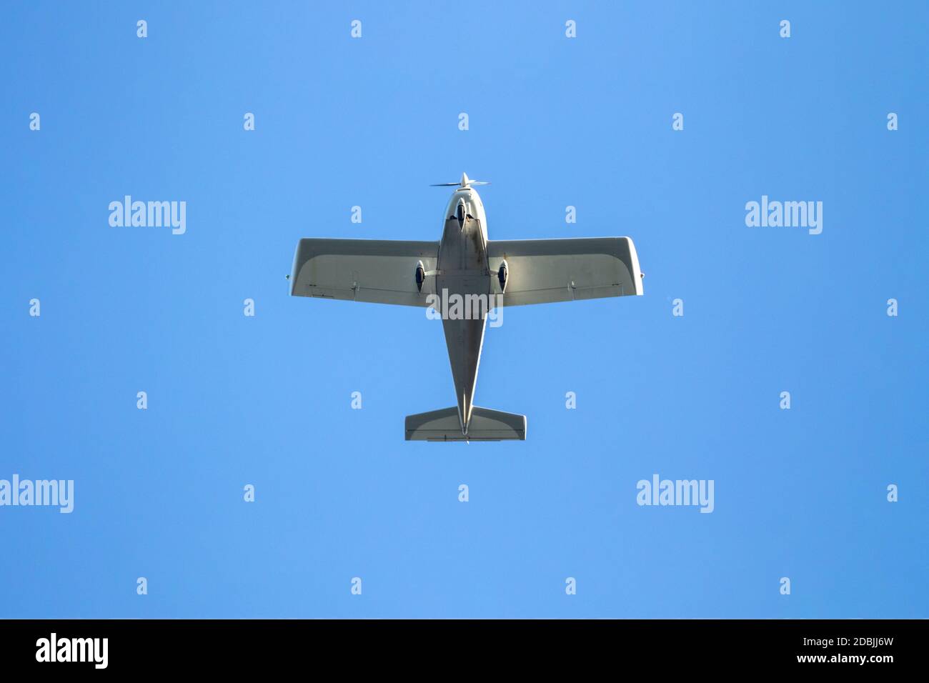 A portrait of a small leisure airplane. You can see the bottom of the aircraft which is flying by with a blue sky. Stock Photo
