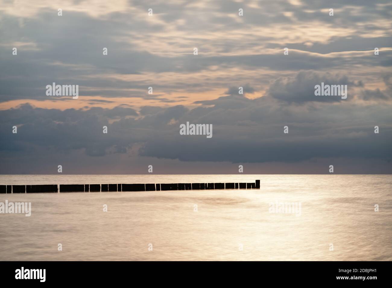 Quiet beach shot of the Baltic Sea coast with a row of groynes parallel to the horizon, the water surface is smoothed by long time exposure, light gre Stock Photo