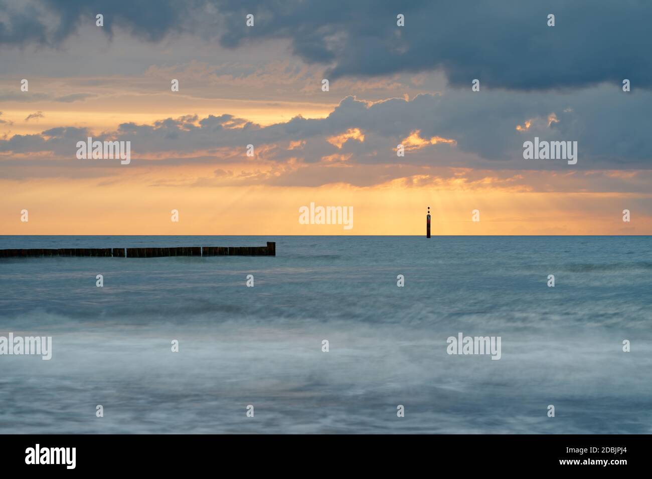 Quiet beach shot from the Baltic Sea coast to the sunset with a distinctive wave structure, a row of groynes and a signal mast in the background, the Stock Photo