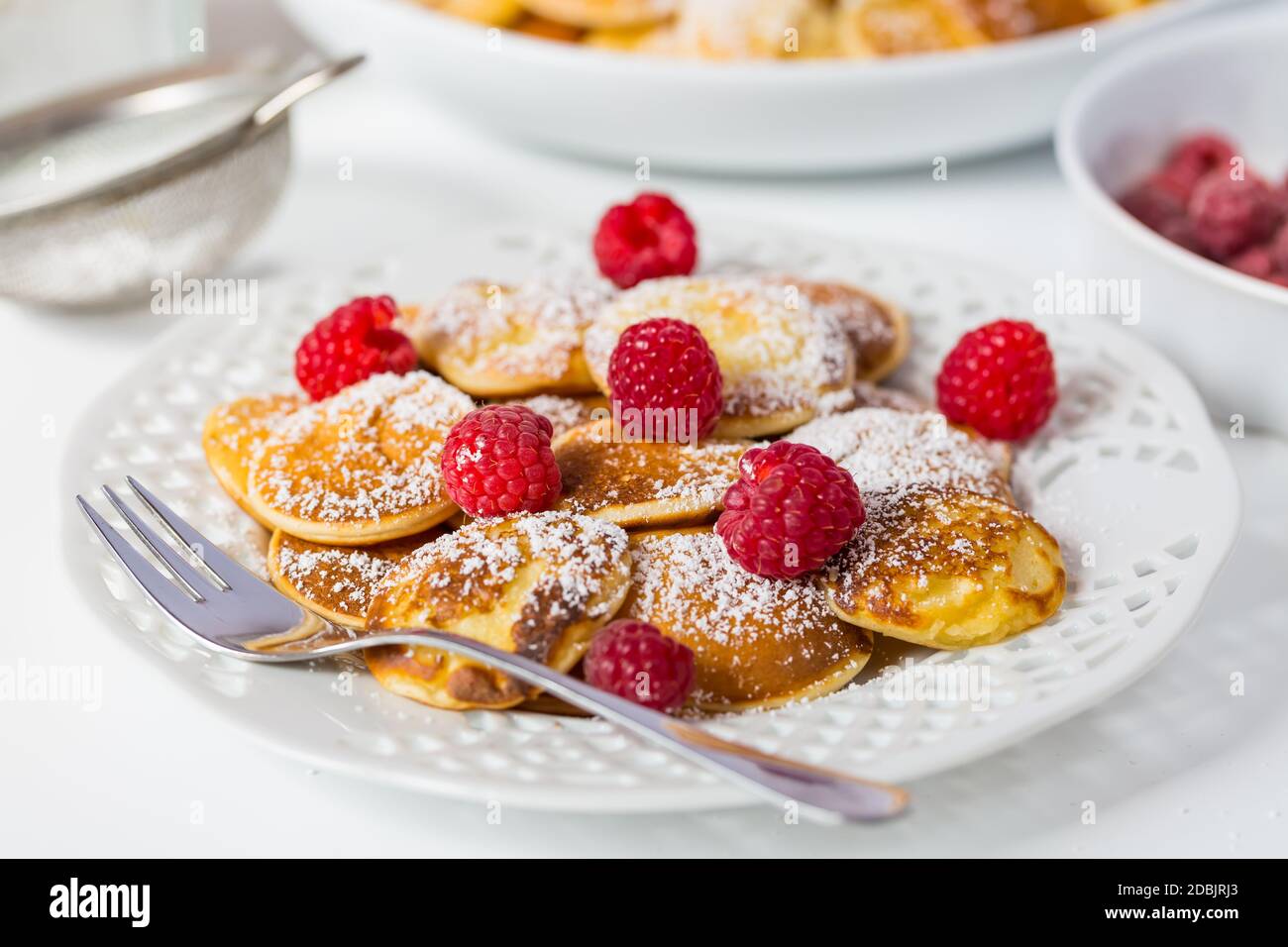 Poffertjes - small Dutch pancakes with fresh raspberries. Traditional Dutch cuisine. Stock Photo