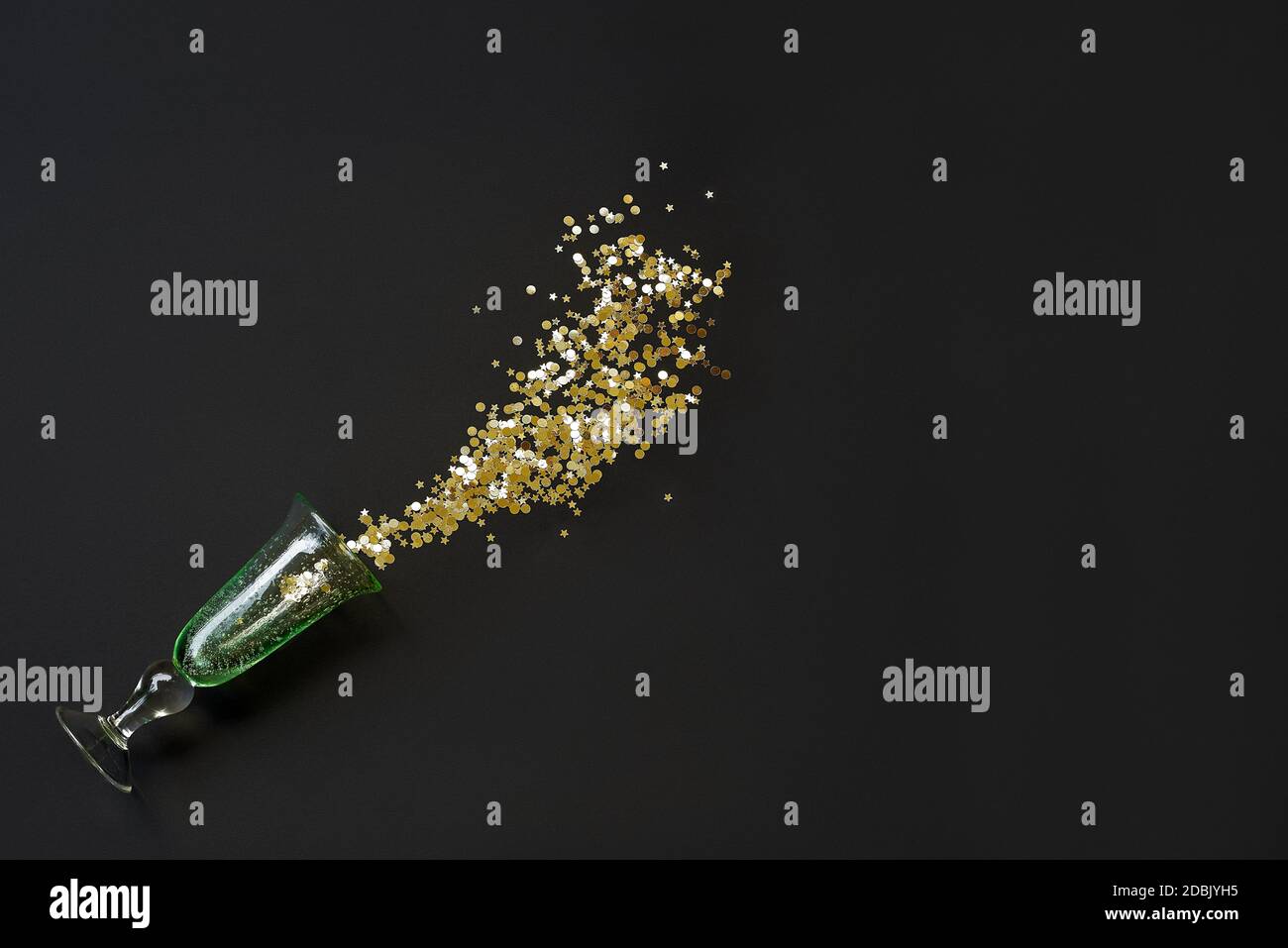 A spilled glass with golden glitter on black background Stock Photo