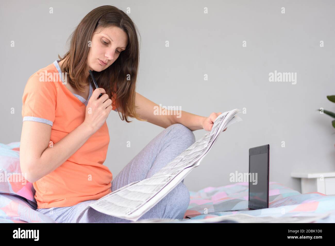 A girl is looking for work looking through ads in the newspaper, next to a laptop Stock Photo