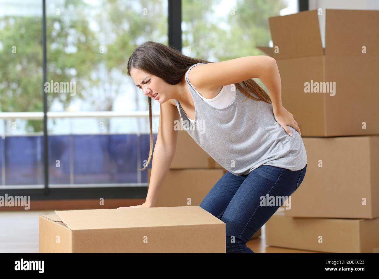 Woman in pain moving boxes suffering backache grabbinng lumbar area at