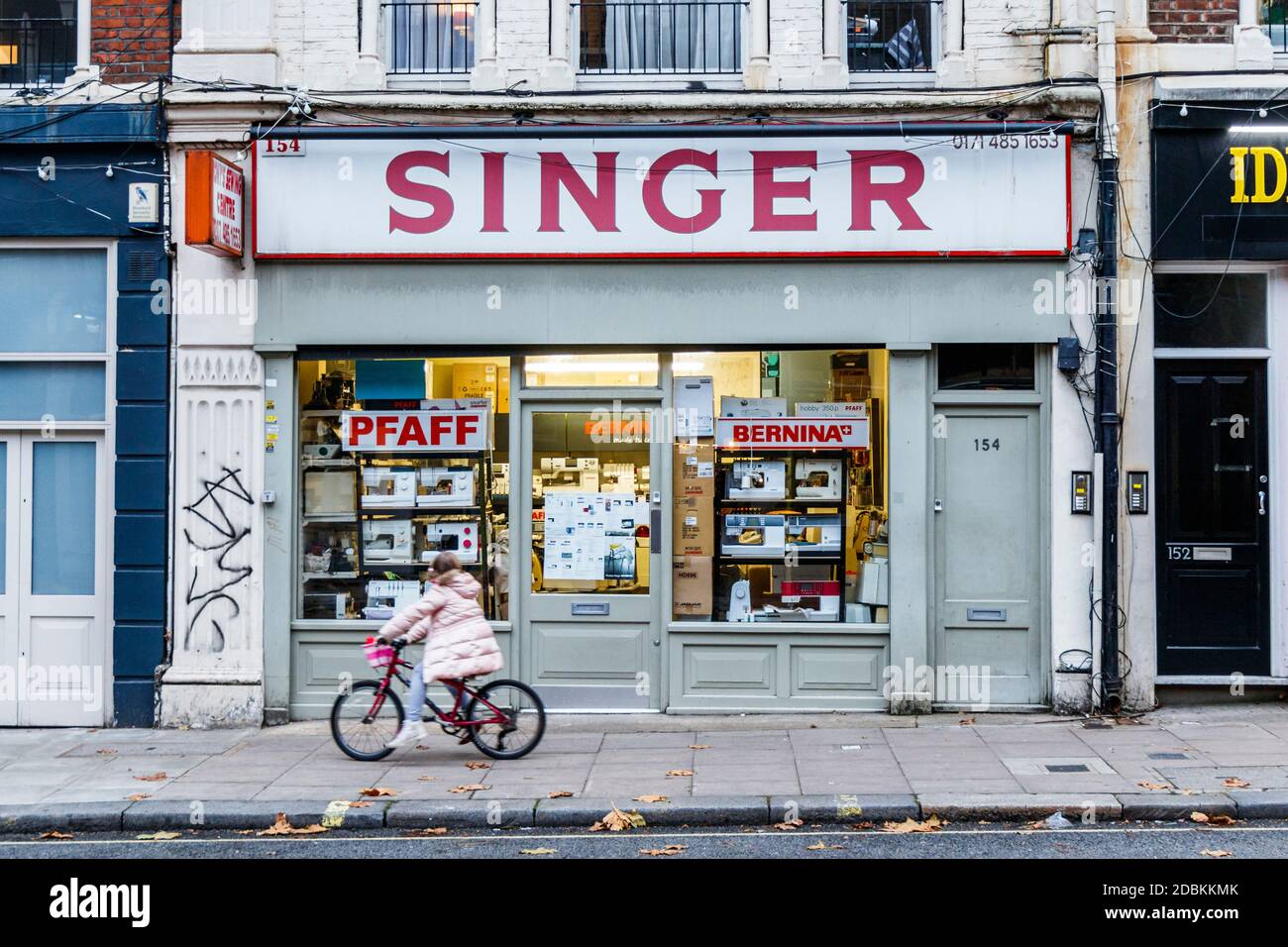 A child on a bicycle cycles past Tony's Singer sewing machine shop in Fortess Road, closed during the second coronavirus pandemic lockdown, London, UK Stock Photo