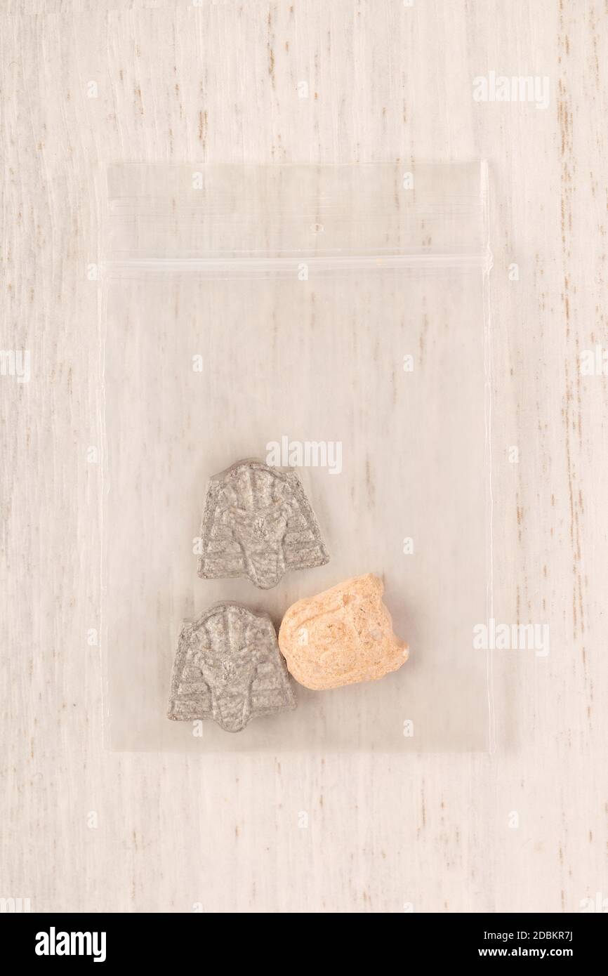 Ecstasy party pill in plastic bag on white wooden background from above. Stock Photo