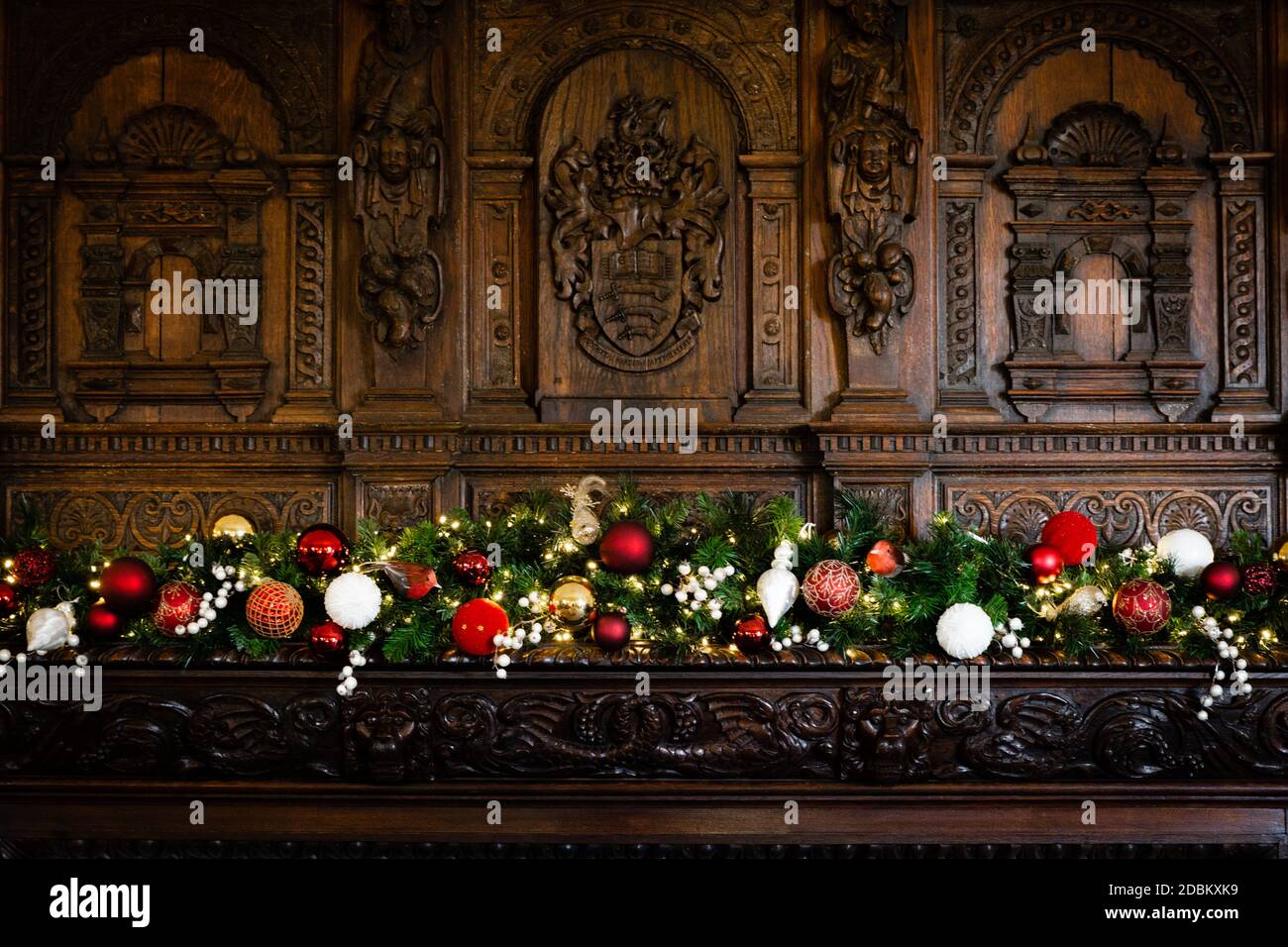 A beautiful traditional wooden fire surround with intricate carvings adorned with a festive Christmas garland of red, green and golds. Stock Photo