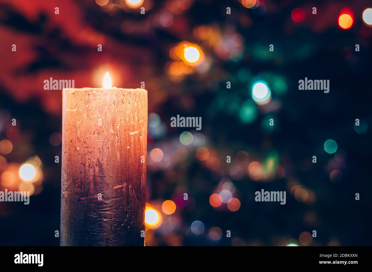 one burning candle concept with shining bokeh glittering ligts on christmas tree on dark background Stock Photo
