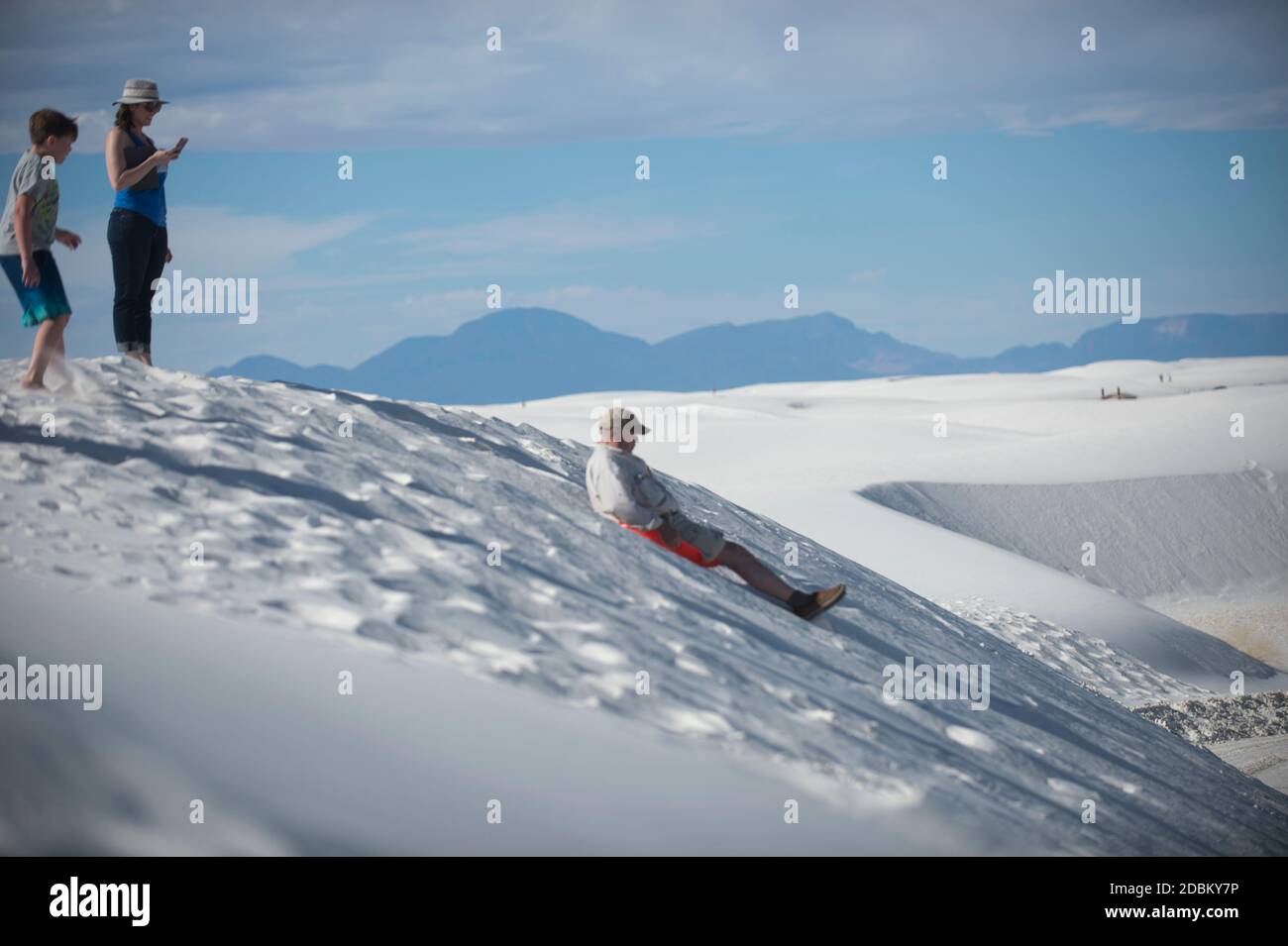 Man sledding down sand dune with family watching, White Sands National Monument, New Mexico, USA Stock Photo