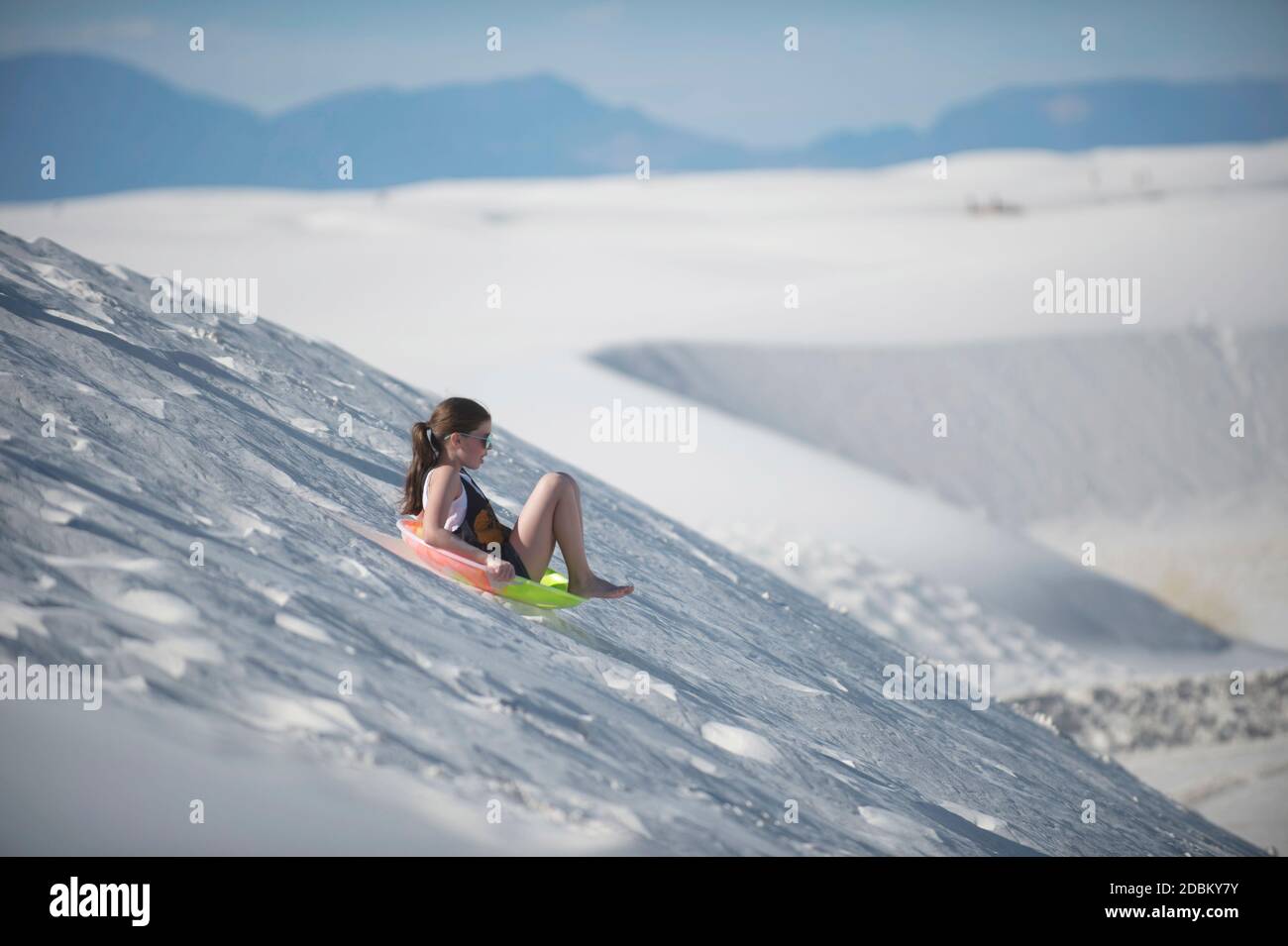 Girl sledding down sand dune, White Sands National Monument, New Mexico, USA Stock Photo