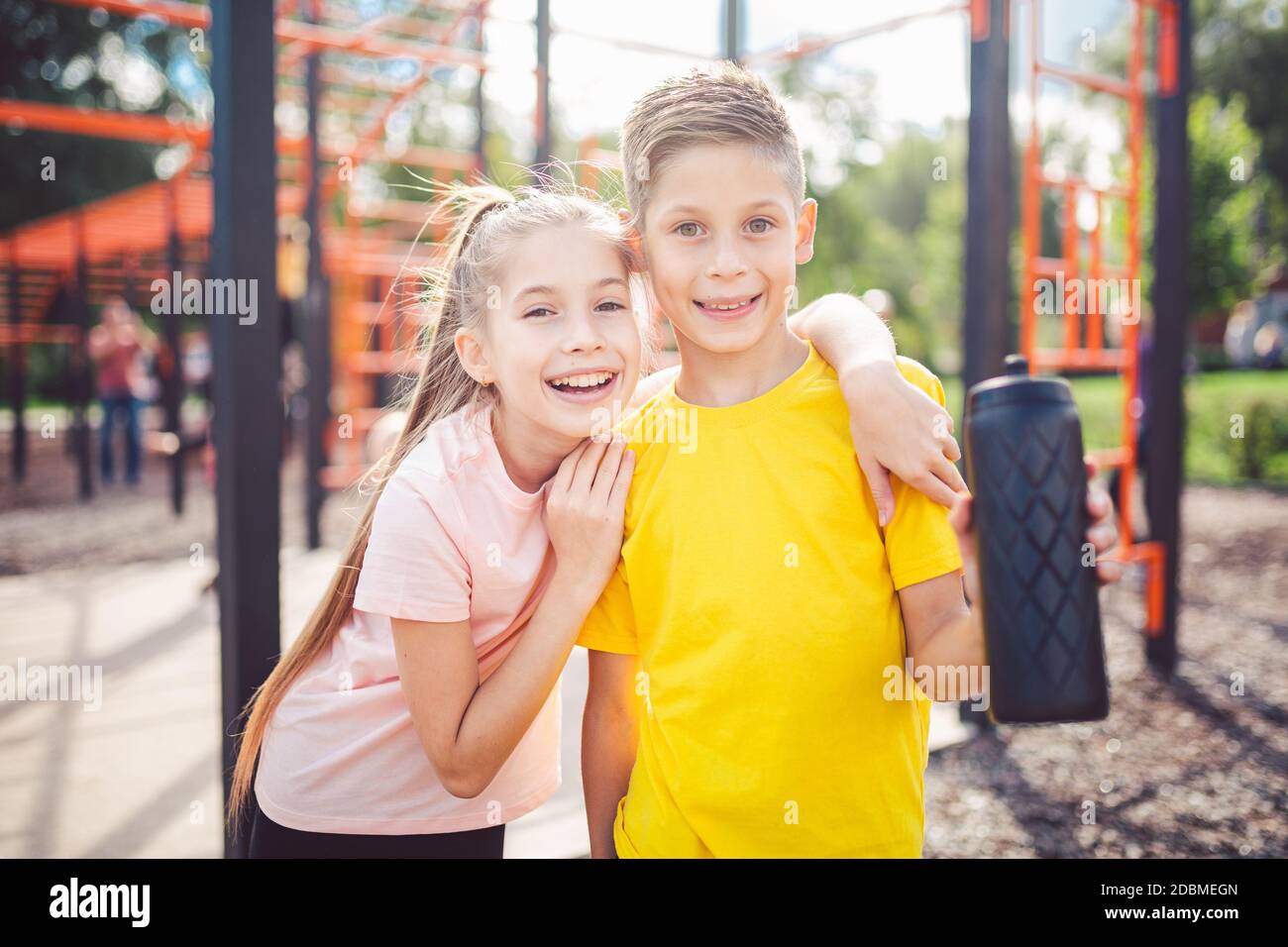 Teens children and sports theme. Two kids athletes twins rest and replenish their thirst during workout outdoor gym workout in sunny summer weather. S Stock Photo