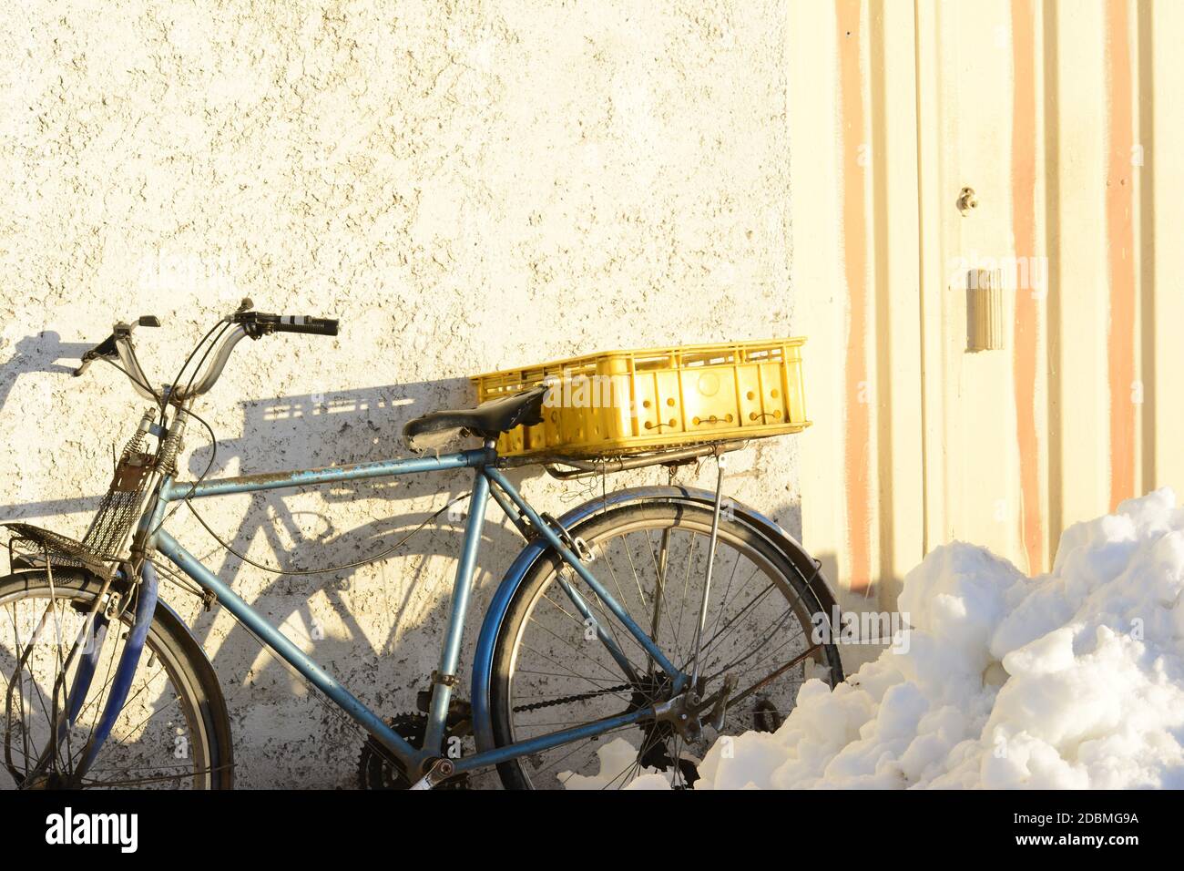An antique bike with an empty yellow pot parked in front of cement wall beside doorway Stock Photo