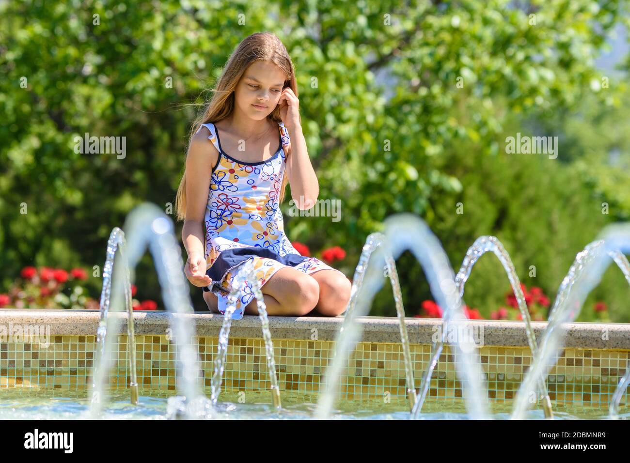 A girl sits at the fountain and looks at the jets of water Stock Photo ...