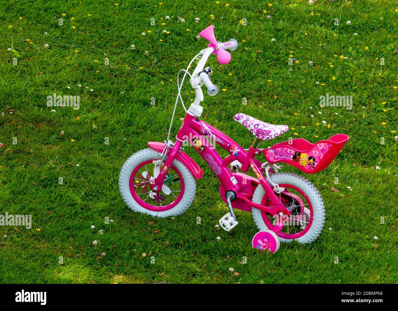 12 inches pink girl's pedal bike with training wheels in open shade on green meadow backyard Stock Photo