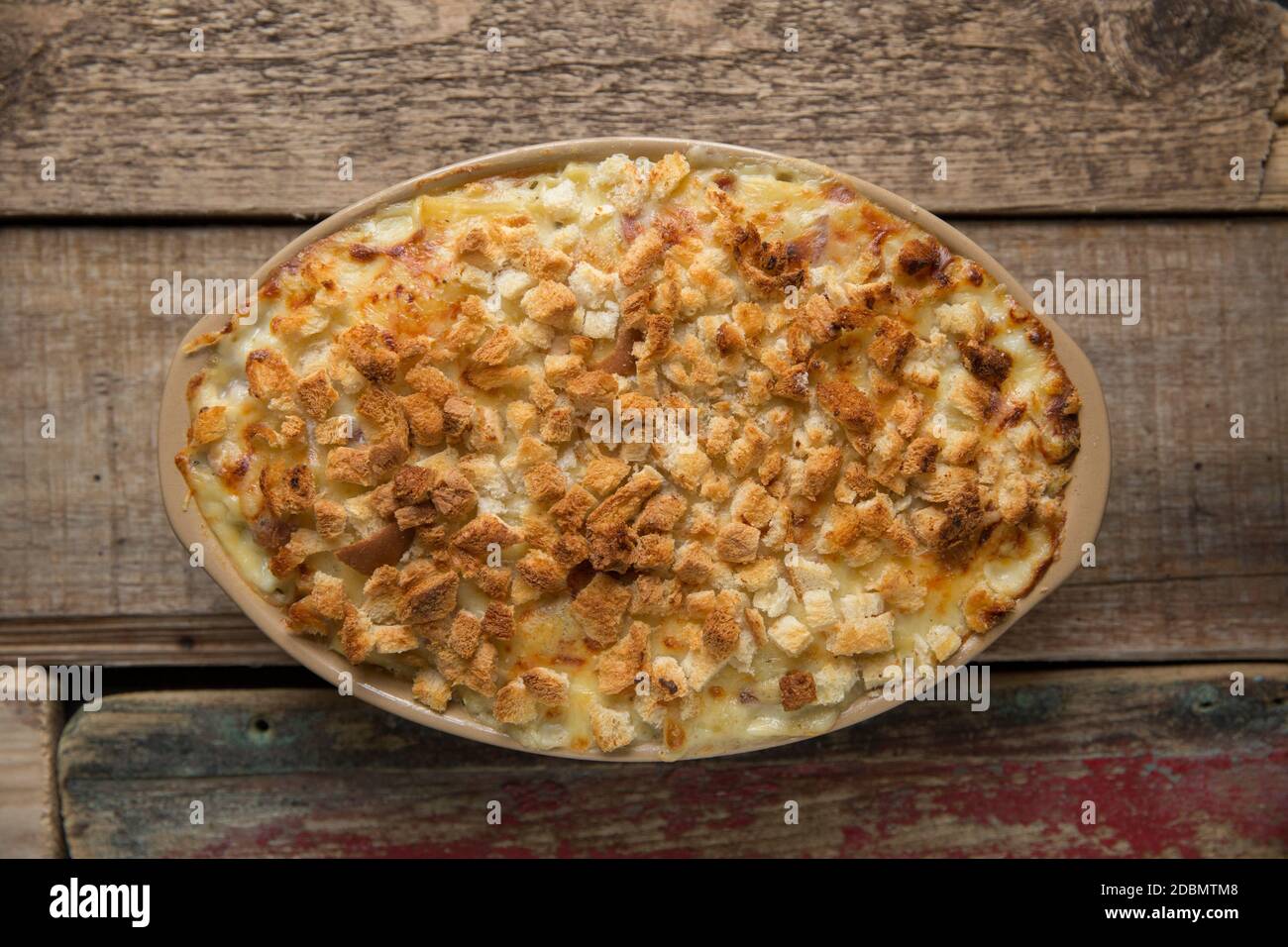 A macaroni cheese that has been made with diced smoked bacon and topped with cubed, toasted bread. Wooden background. England UK GB Stock Photo