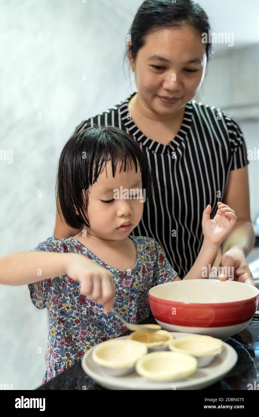 Asian girl cooking egg tart bakery with her mom, housework for child make executive function for kid. Houseworking food lifstyle and family concept. Stock Photo