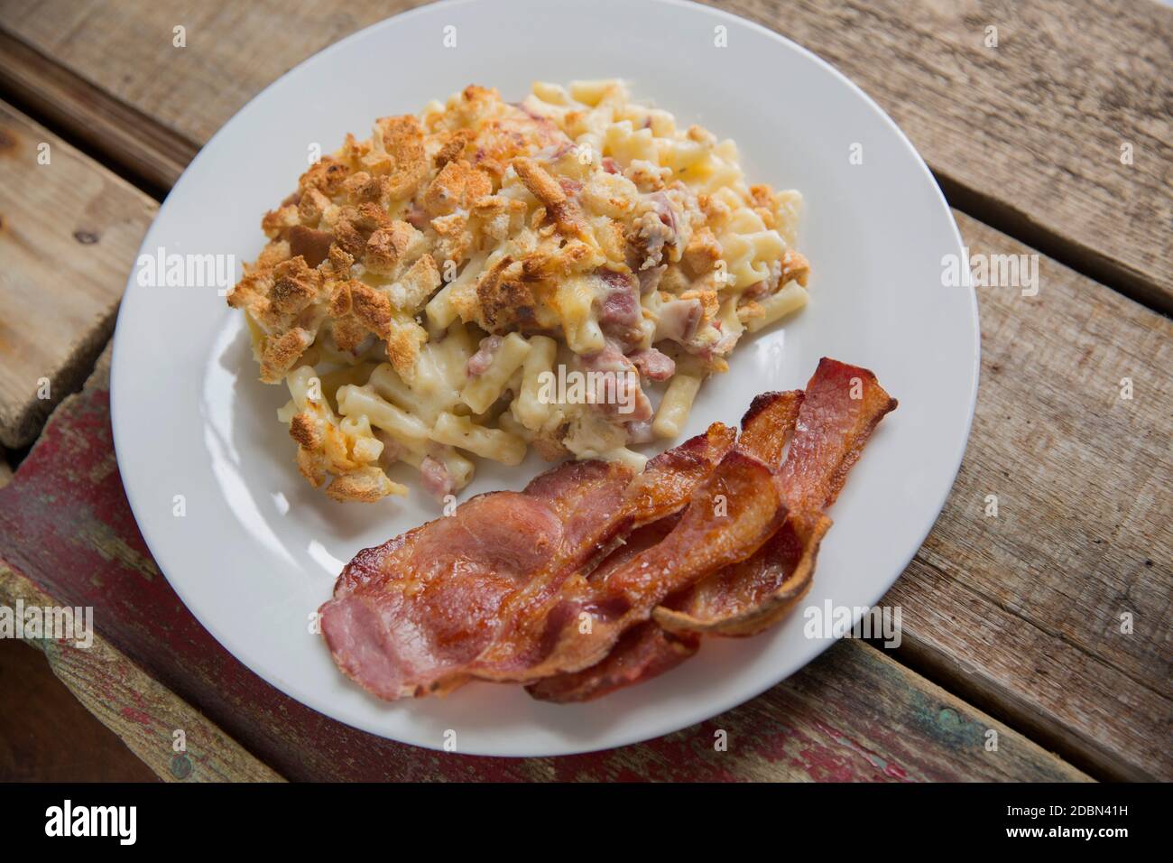 A macaroni cheese that has been made with diced smoked bacon and topped with cubed, toasted bread. Additional rashers of grilled smoky bacon have been Stock Photo