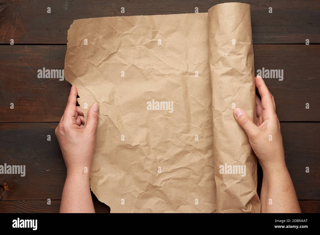 two female hands hold a rolled roll of brown craft paper on a wooden table, top view Stock Photo