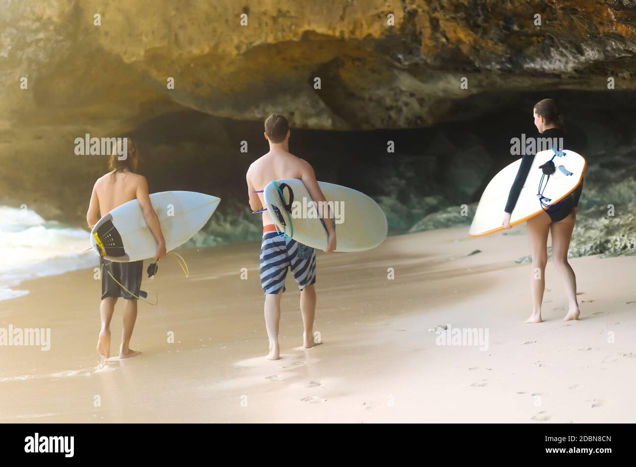 Three people with surfboards on beach, Uluwatu, Bali, Indonesia Stock