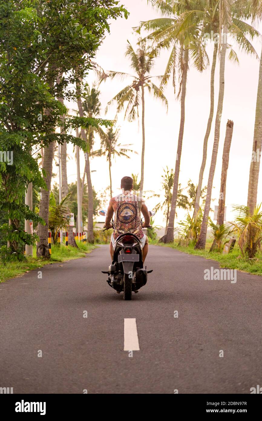 Man riding motorcycle along empty highway, Bali, Indonesia Stock Photo