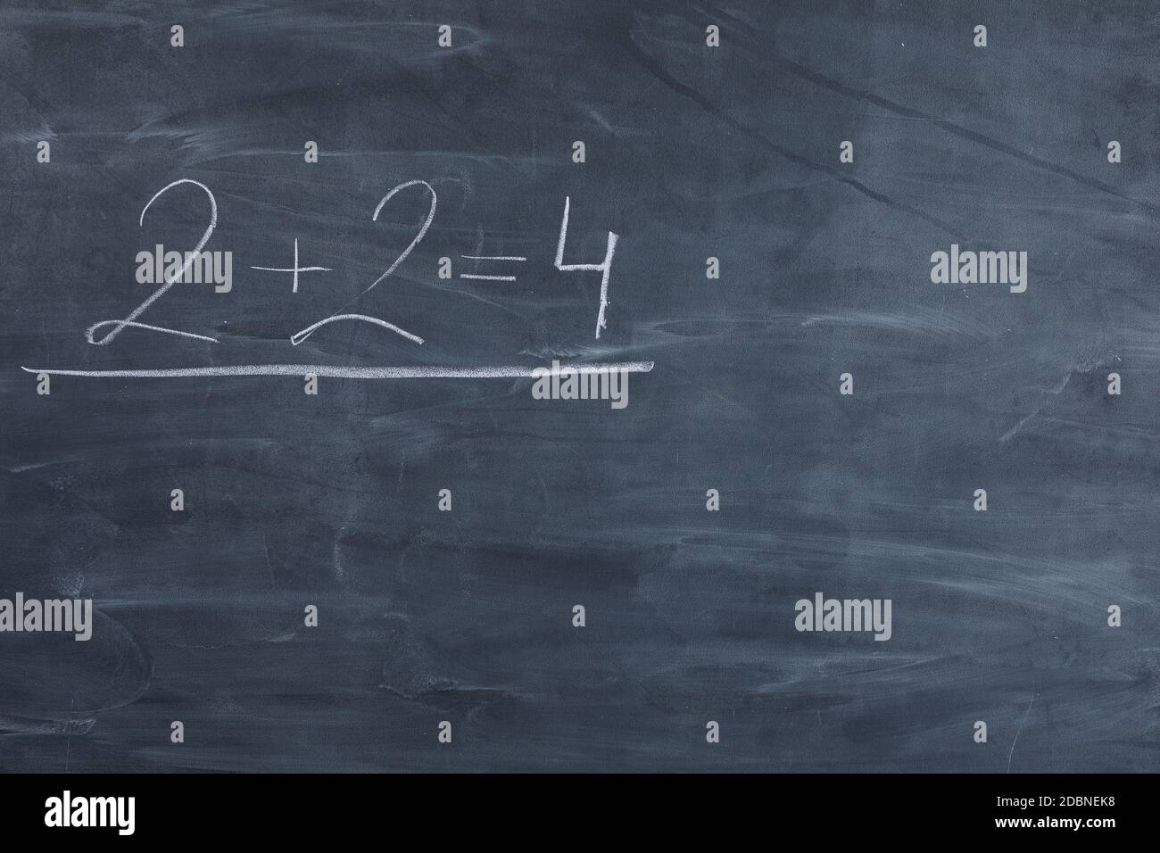 It's written in white chalk on a blackboard - two plus two equals four. The basics of arithmetic start with the youngest grades in every school in the world. Stock Photo