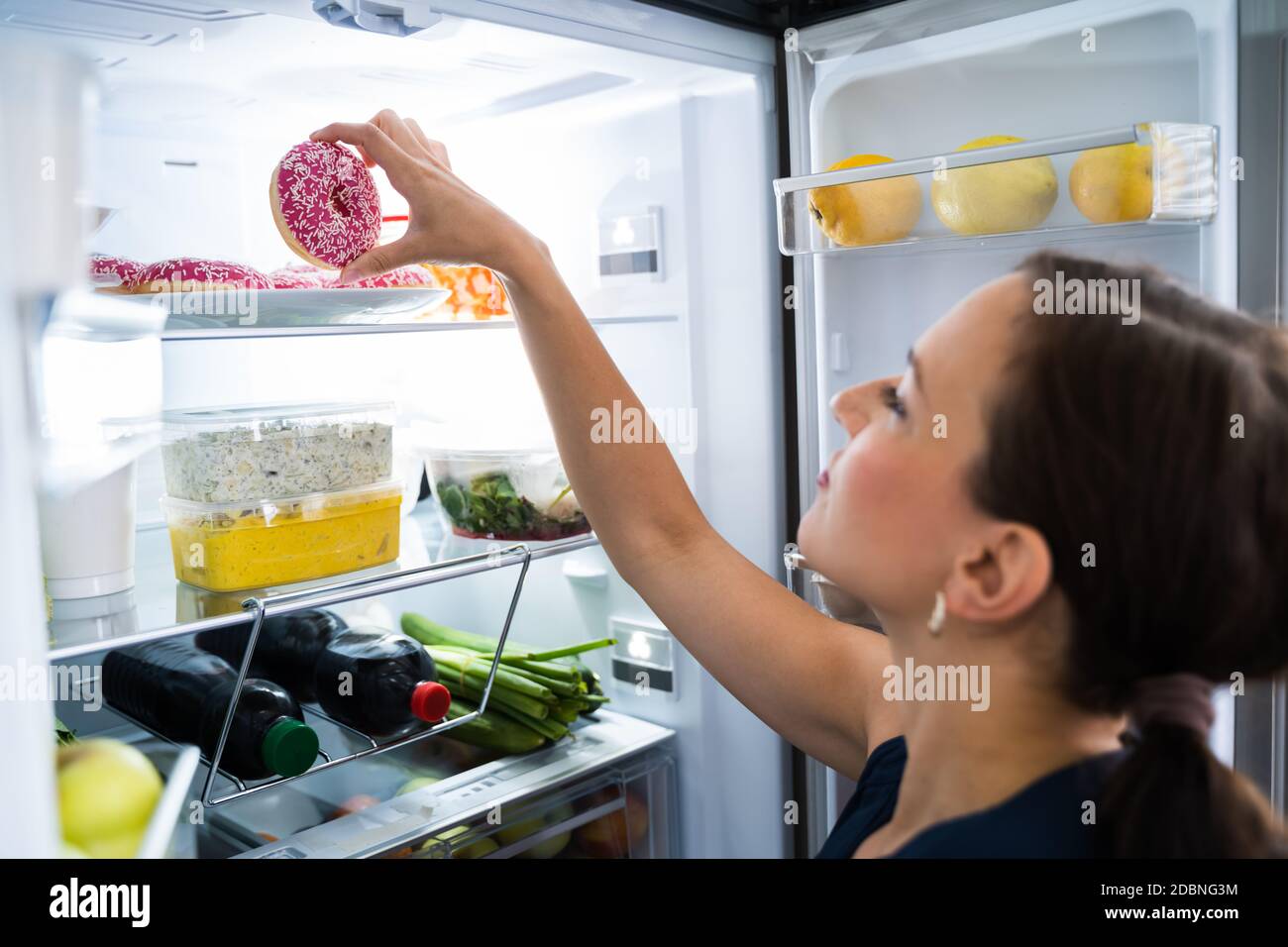 Woman On Diet Indulging In Kitchen Near Refrigerator Stock Photo