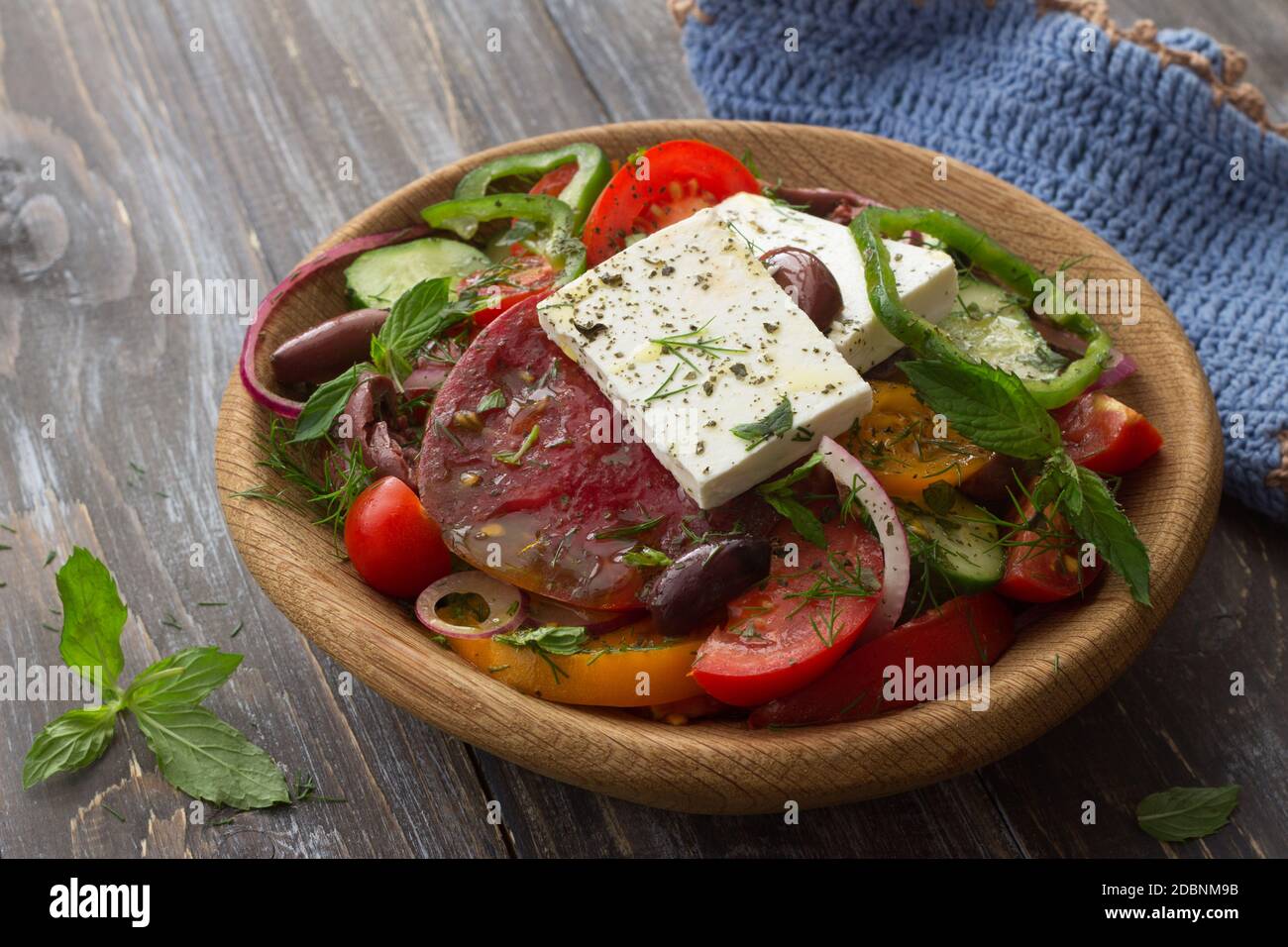 Homemade Greek salad from tomatoes, cucumbers, sweet peppers, cheese, olives and greens in a wooden bowl on a wooden table. Healthy delicious food Stock Photo