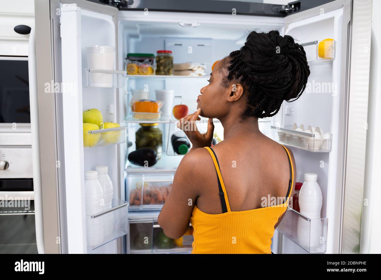 African Woman Think About Food Near Fridge In Kitchen Stock Photo