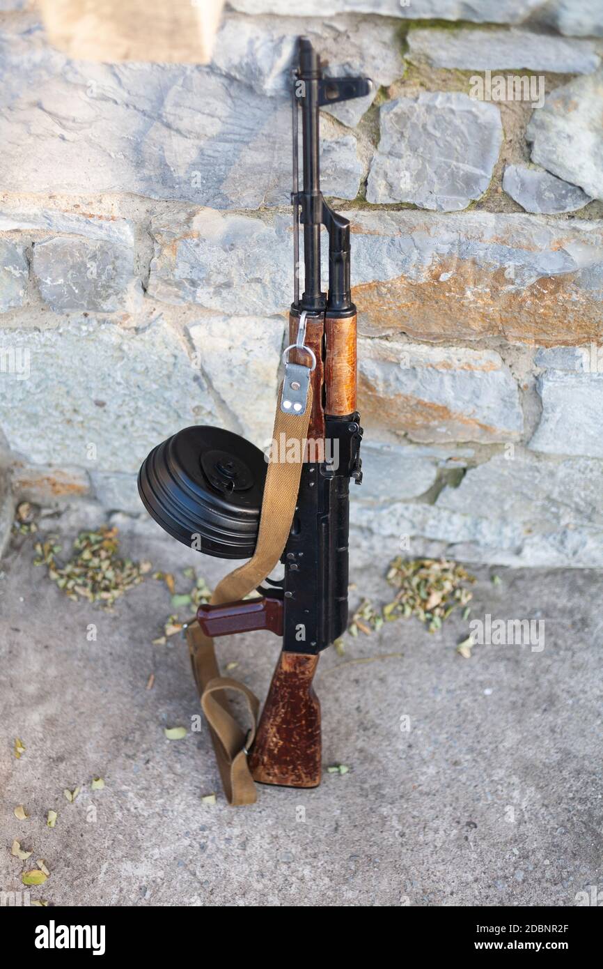 Kalashnikov AKM with high-capacity 75 rounds drum magazine near a stone wall Stock Photo