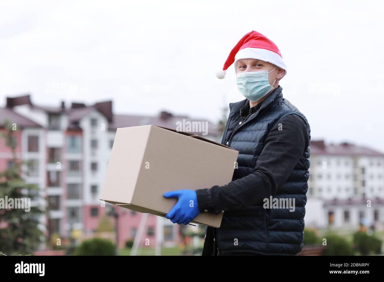 Delivery man in protective mask, gloves and santa's hat holding