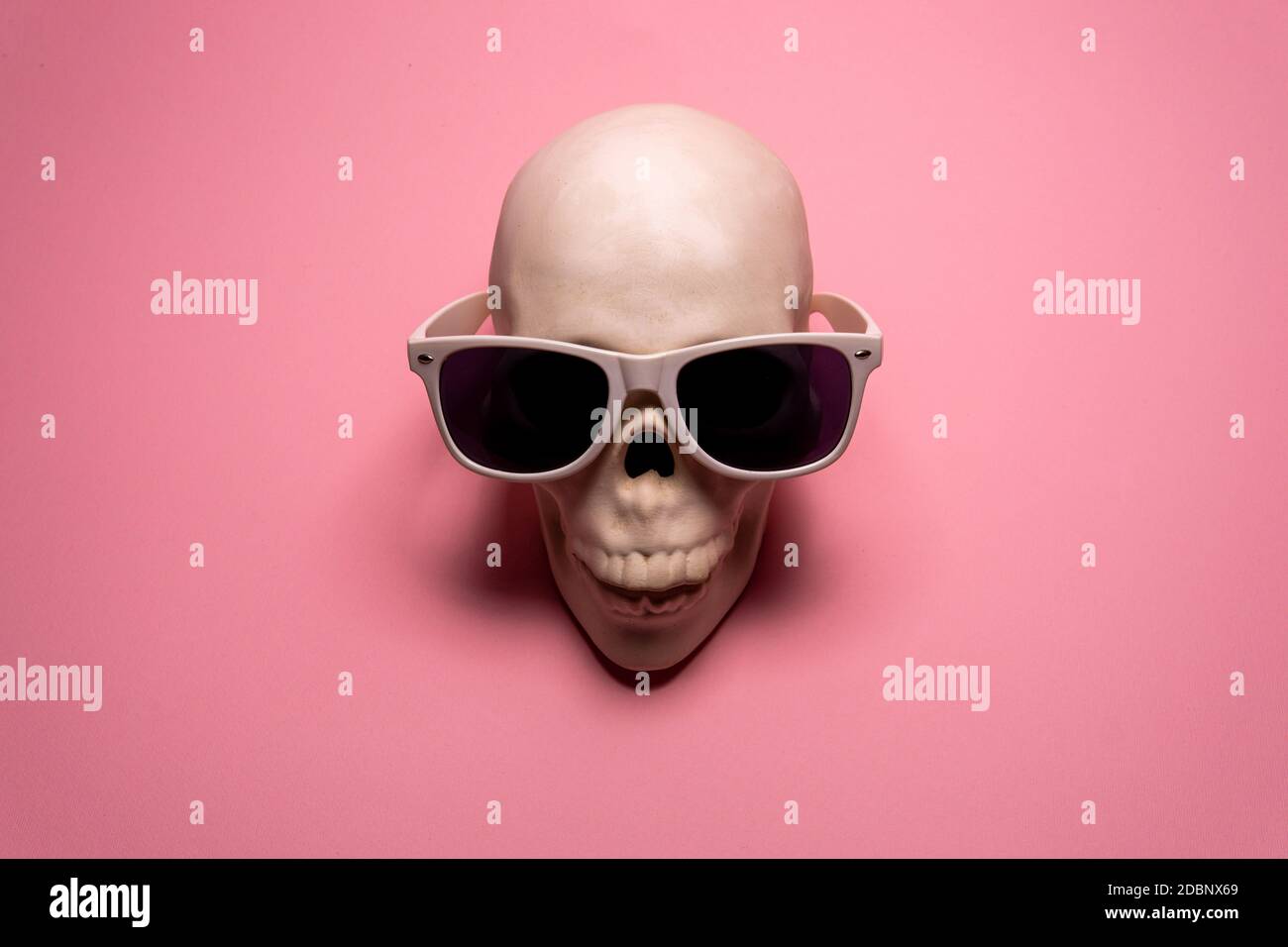 White skull with white sunglasses on pink background. Creative minimal wallpaper Stock Photo