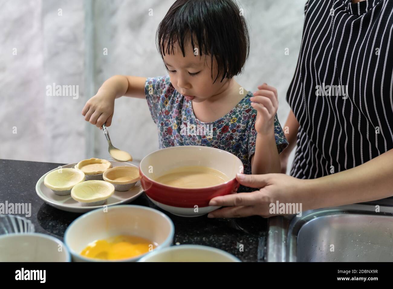 Asian girl cooking egg tart bakery with her mom, housework for child make executive function for kid. Houseworking food lifstyle and family concept. Stock Photo