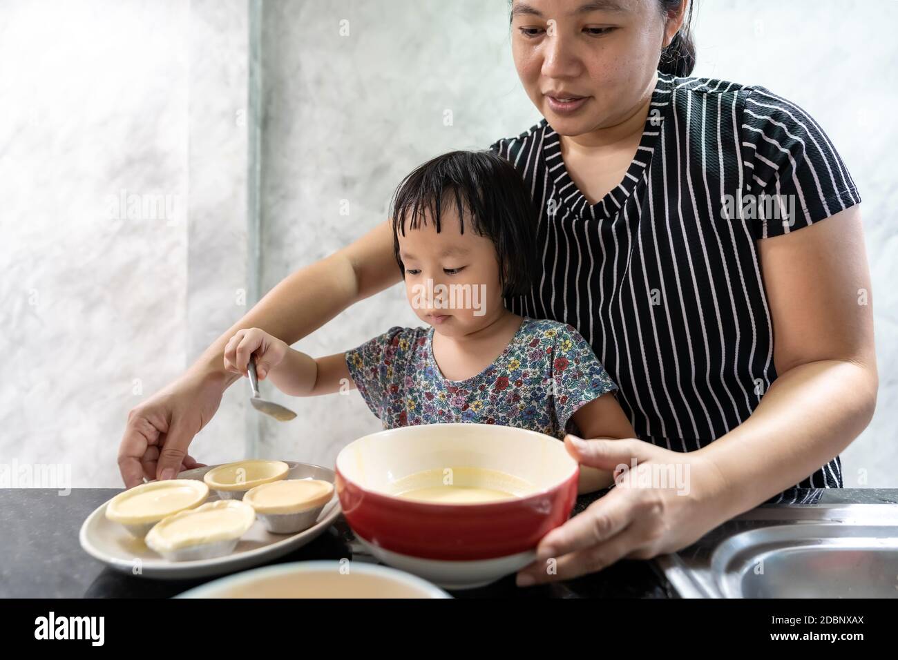 Asian girl cooking egg tart bakery with her mom, housework for child make executive function for kid. Houseworking food lifstyle and family concept. Stock Photo