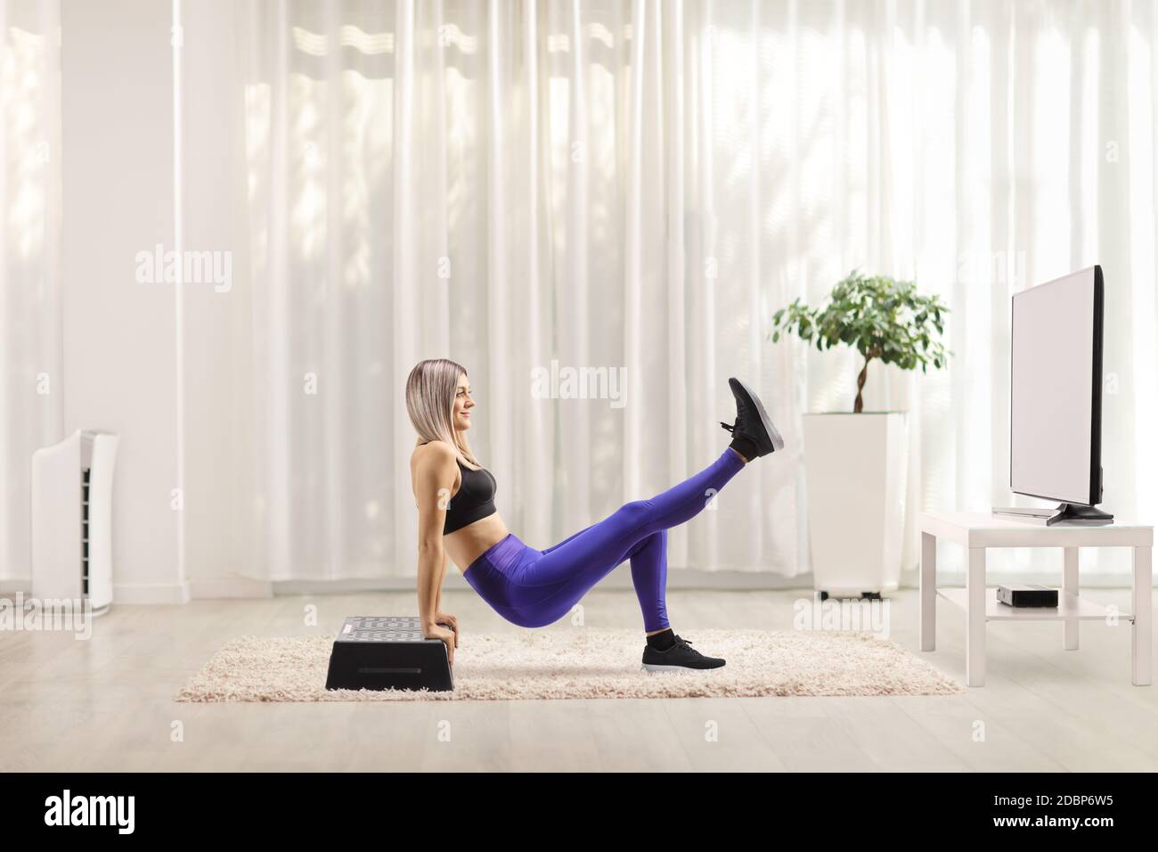 Young woman exercising step aerobic at home in front of tv Stock Photo