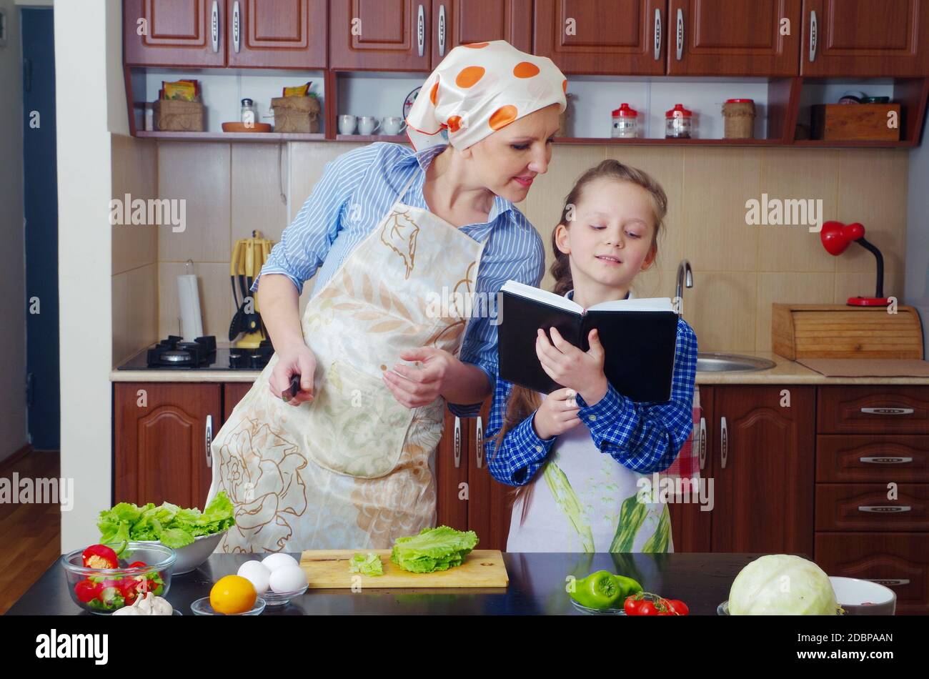 Little Girl Is Teaching Her Mother To Cook In A Kitchen With Different little-girl-is-teaching-her-mother-to-cook-in-a-kitchen-with-different
