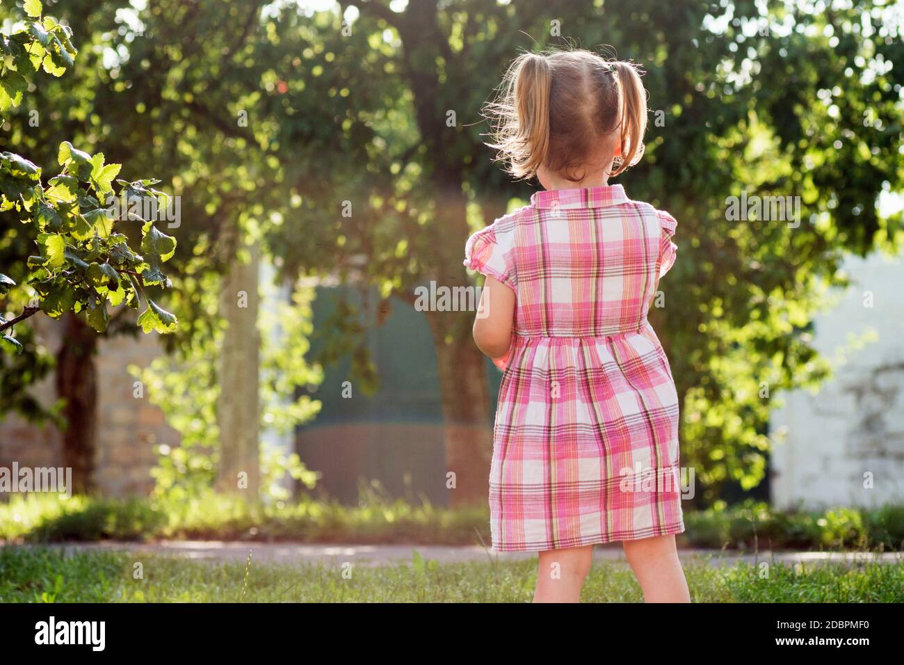 The cute little girl in pink dress is standing on the street outdoors
