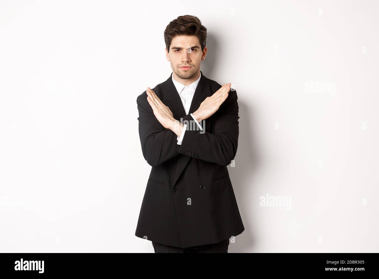 Portrait of serious and concerned man in black suit, showing stop gesture and frowning, making cross to prohibit or decline something, standing over Stock Photo