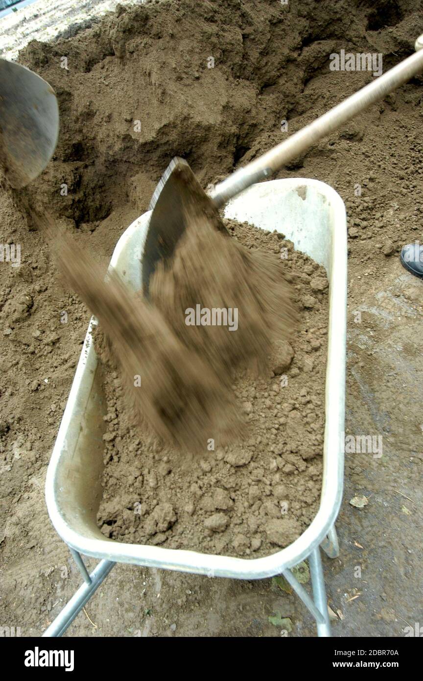 shovel filling a wheelbarrow with sand at the construction site Stock